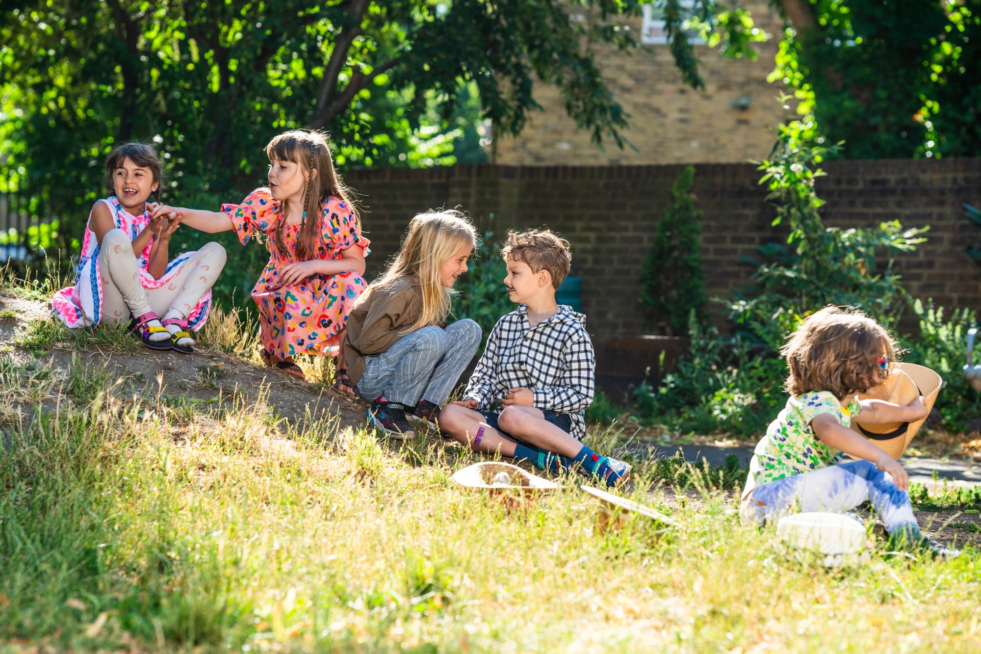 Group of children sat on a slope of earth, laughing and chatting